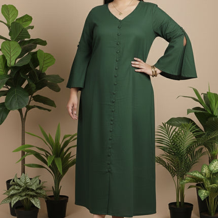 Woman wearing a green dress standing in front of potted plants on a beige background
