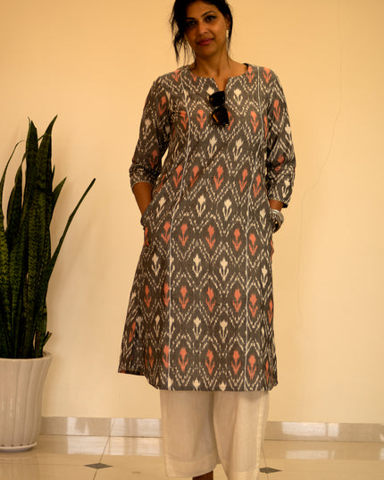 Woman wearing a patterned kurta with white pants standing indoors next to a plant.