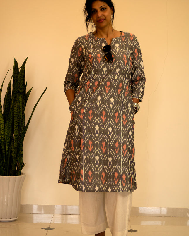 Woman wearing a patterned kurta with white pants standing indoors next to a plant.
